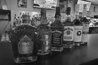 Black and white: Six distinct liquor bottles on a bar counter.