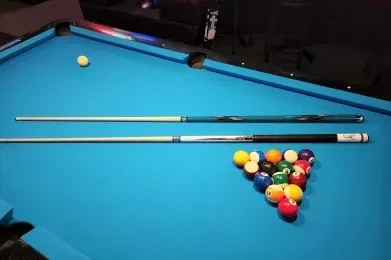 Blue billiard table, racked balls, two pool cues, white cue ball.