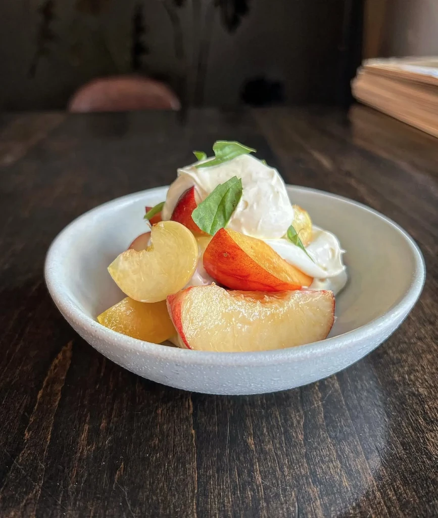 Fresh peach slices, creamy topping, and green leaves in a rustic bowl.
