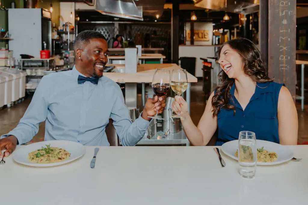 Man and woman smiling, toasting red and white wine in restaurant.