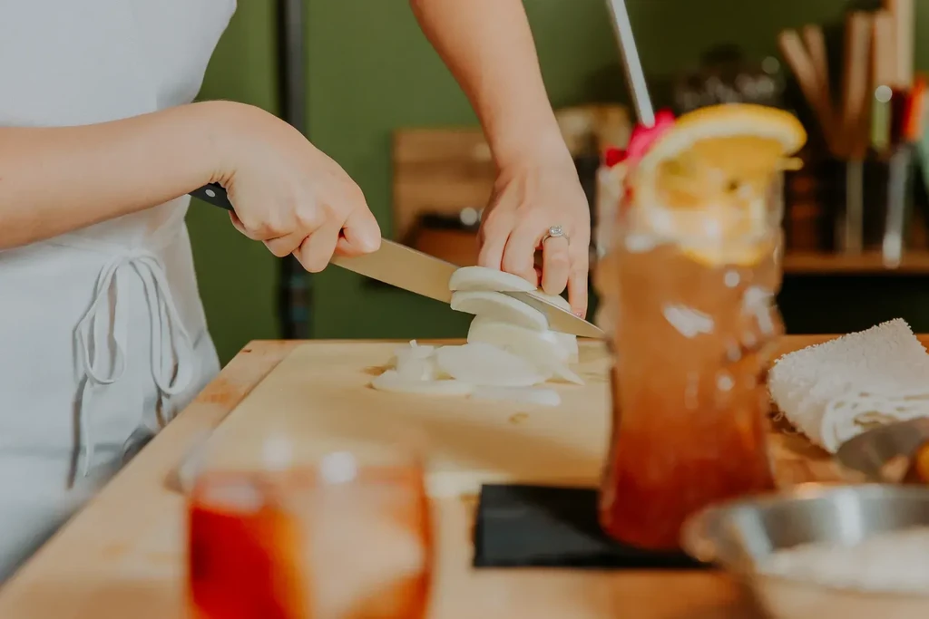 Close-up of hands slicing white onions on a wooden cutting board.