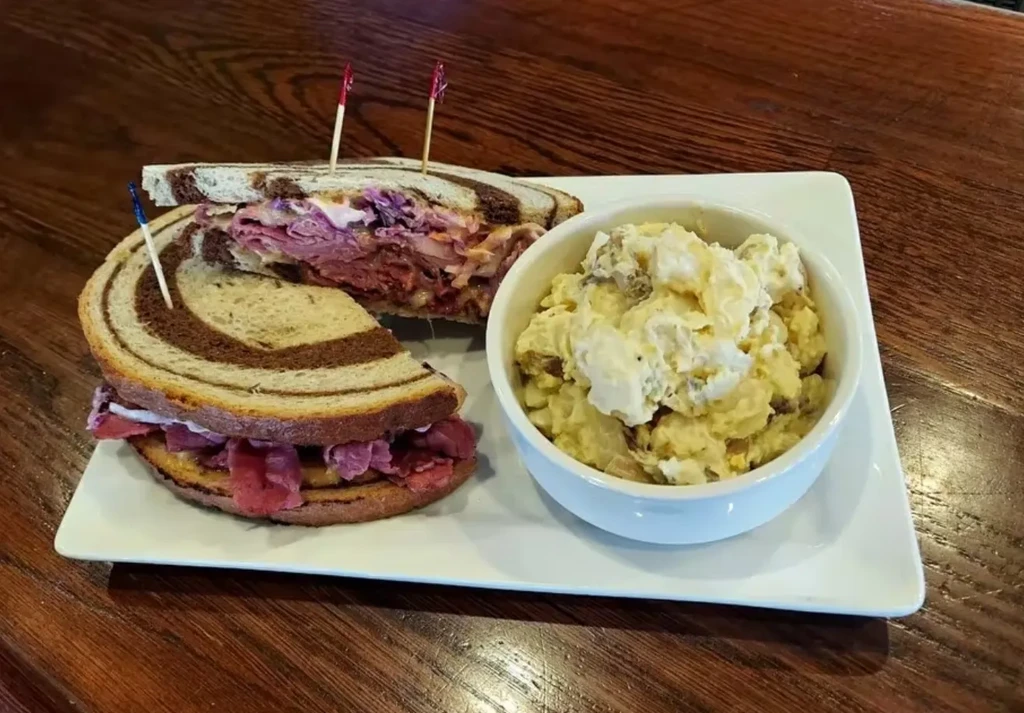 Reuben-style sandwich with potato salad on a dark wooden table.