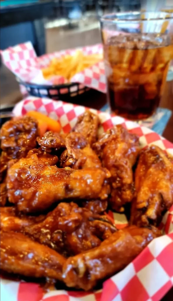 Overflowing basket of sauced chicken wings, carrots, fries, and cola.