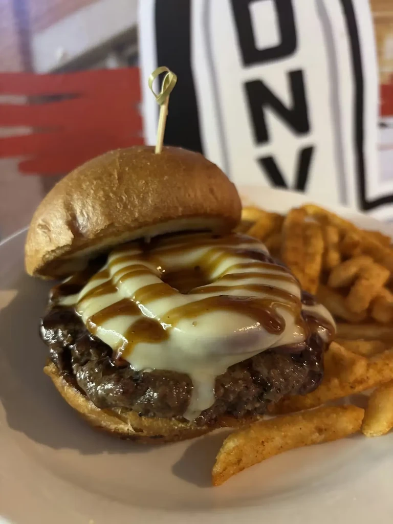 Close-up of a gourmet burger with melted cheese, dark sauce, and crinkle fries.