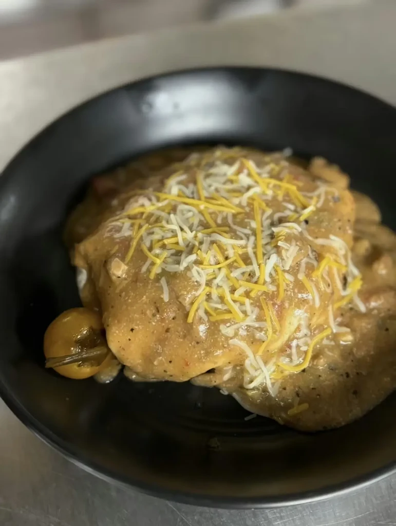 Smothered dish in black bowl with chunky sauce, cheese, and pepper.