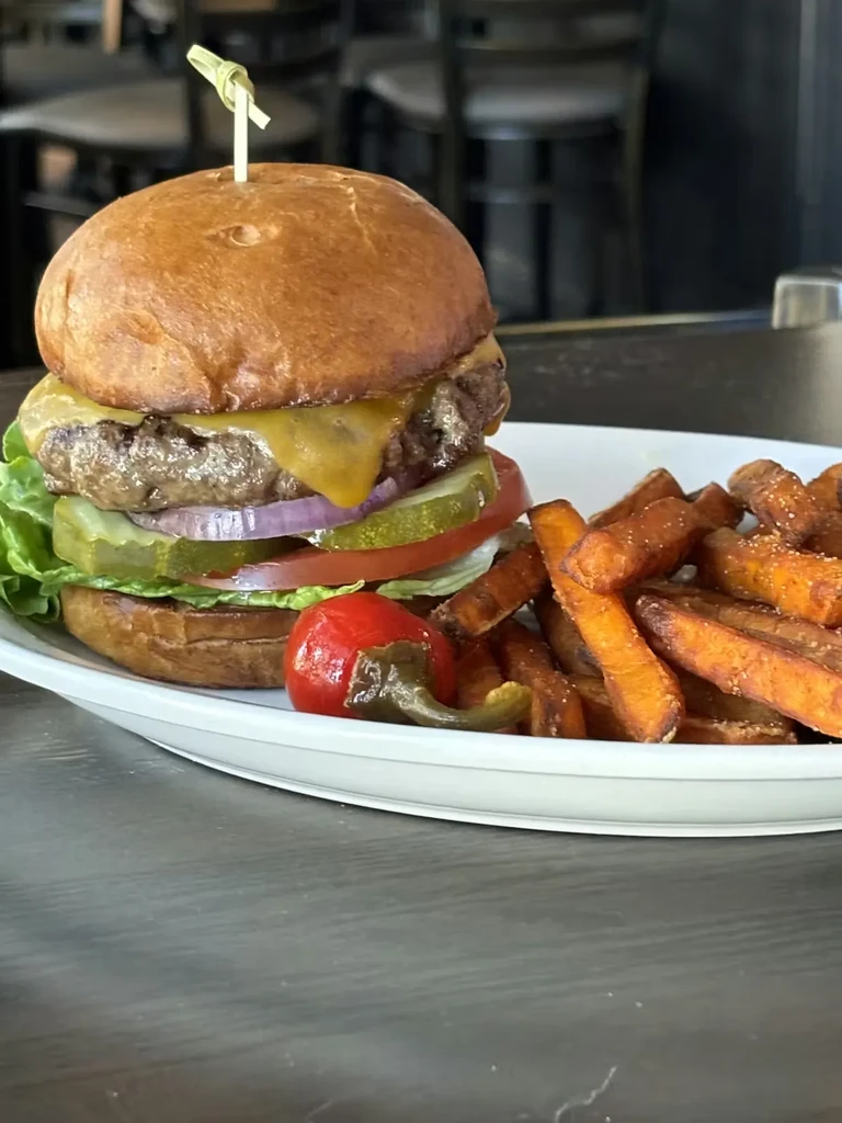 Gourmet cheeseburger, sweet potato fries, and red chili pepper on a plate.