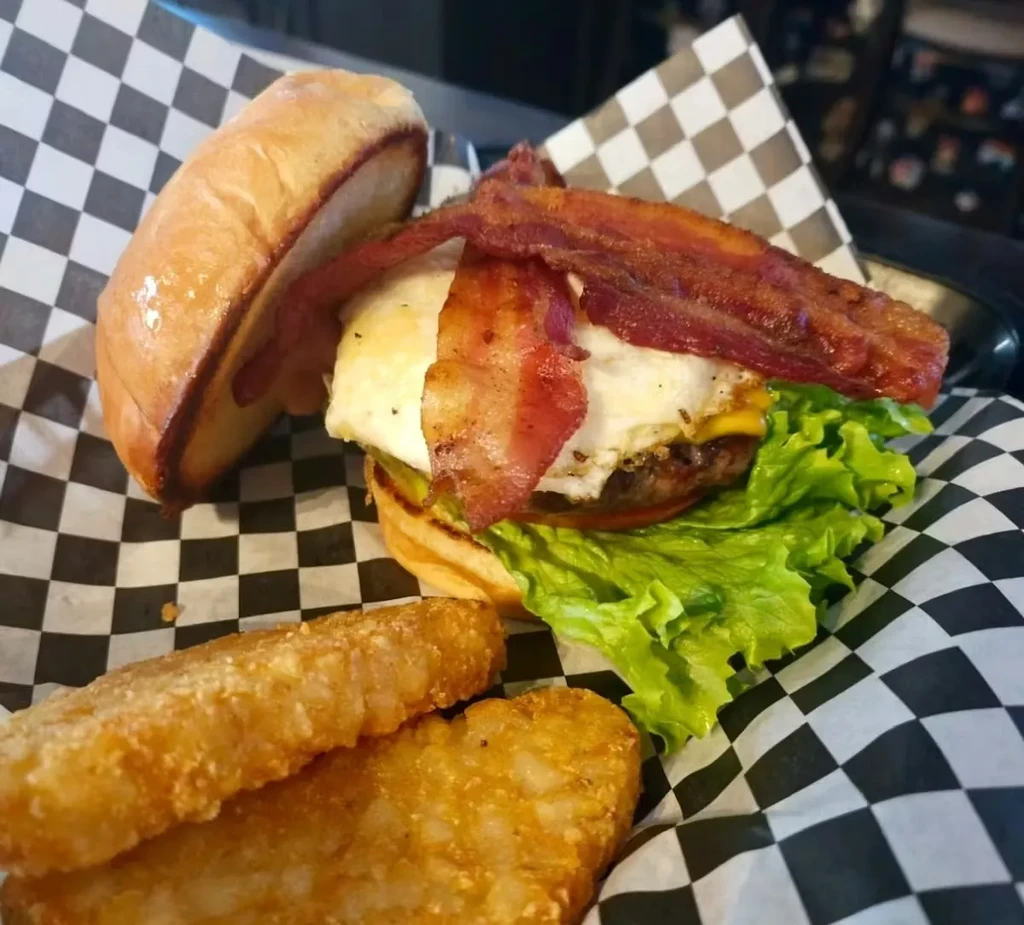 Gourmet burger with egg, bacon, cheese, lettuce, tomato, and hash browns.