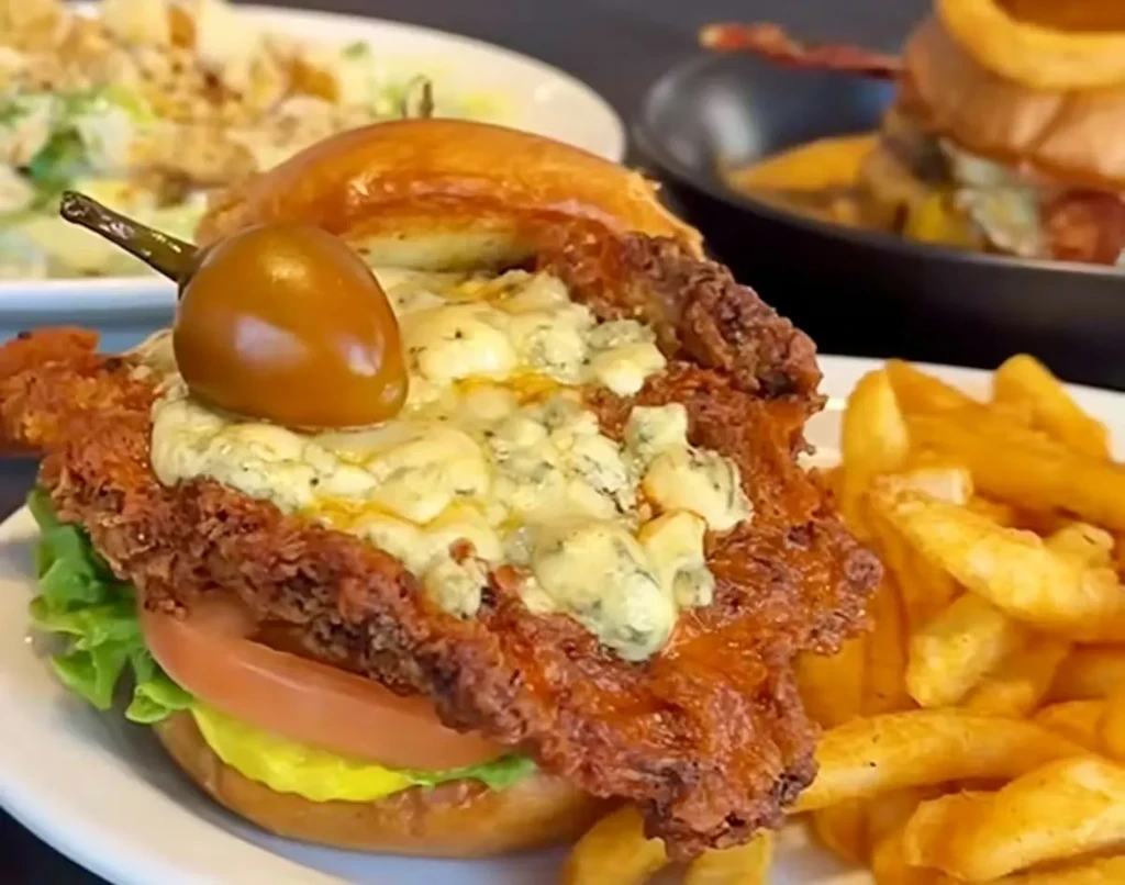 Fried chicken sandwich with blue cheese, lettuce, tomato, fries, and pepper.