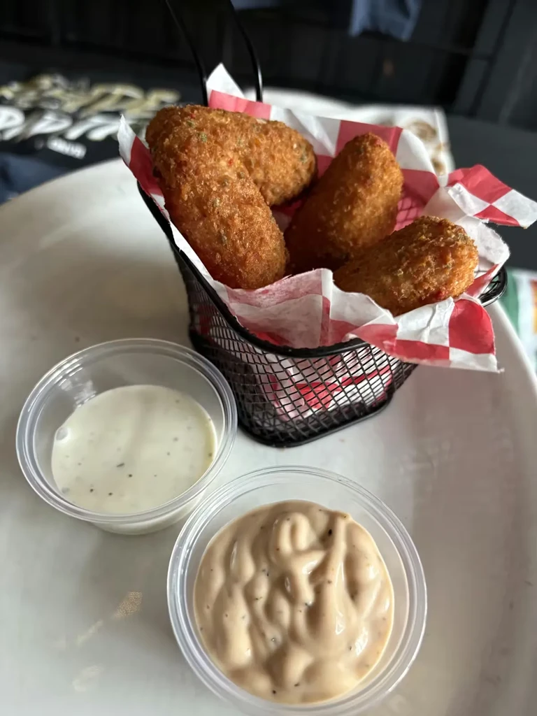 Four crispy fried appetizers in a basket with two dipping sauces.