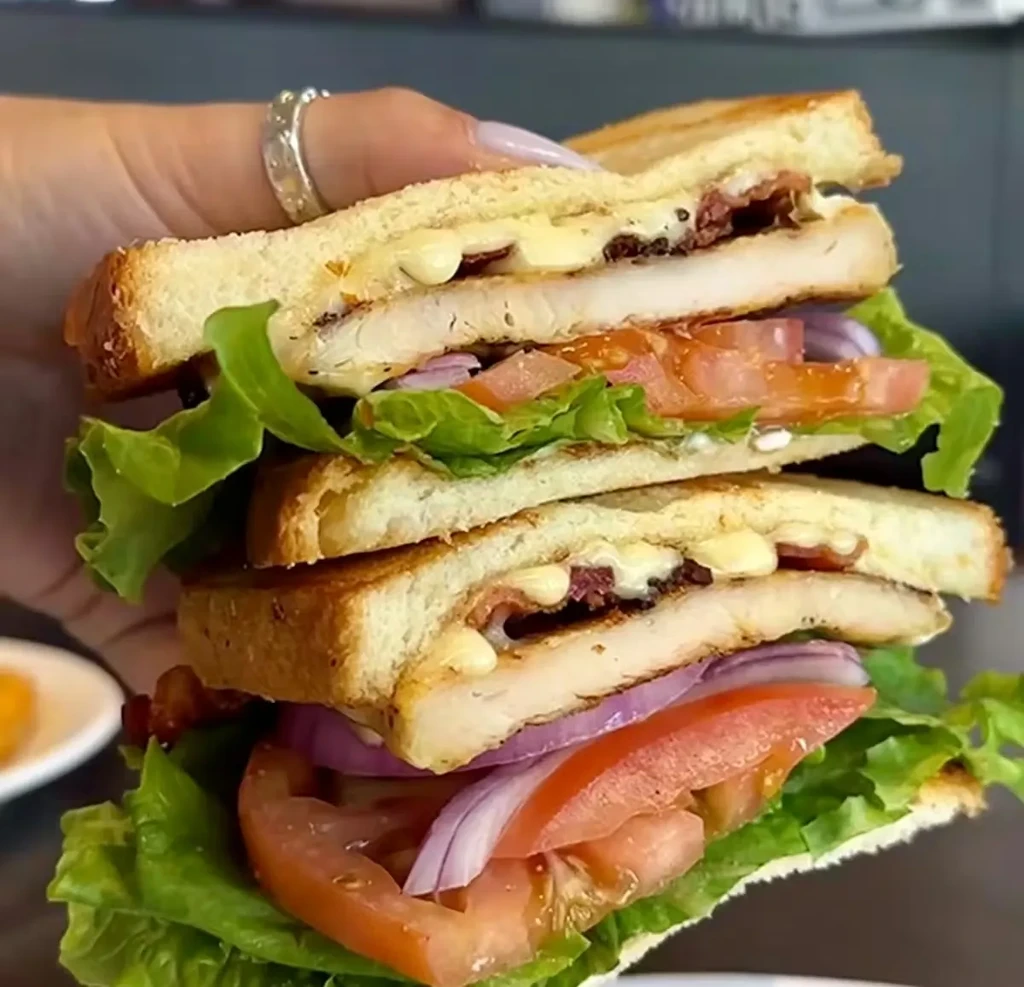 Detailed club sandwich with chicken, bacon, lettuce, tomato, held by hand.