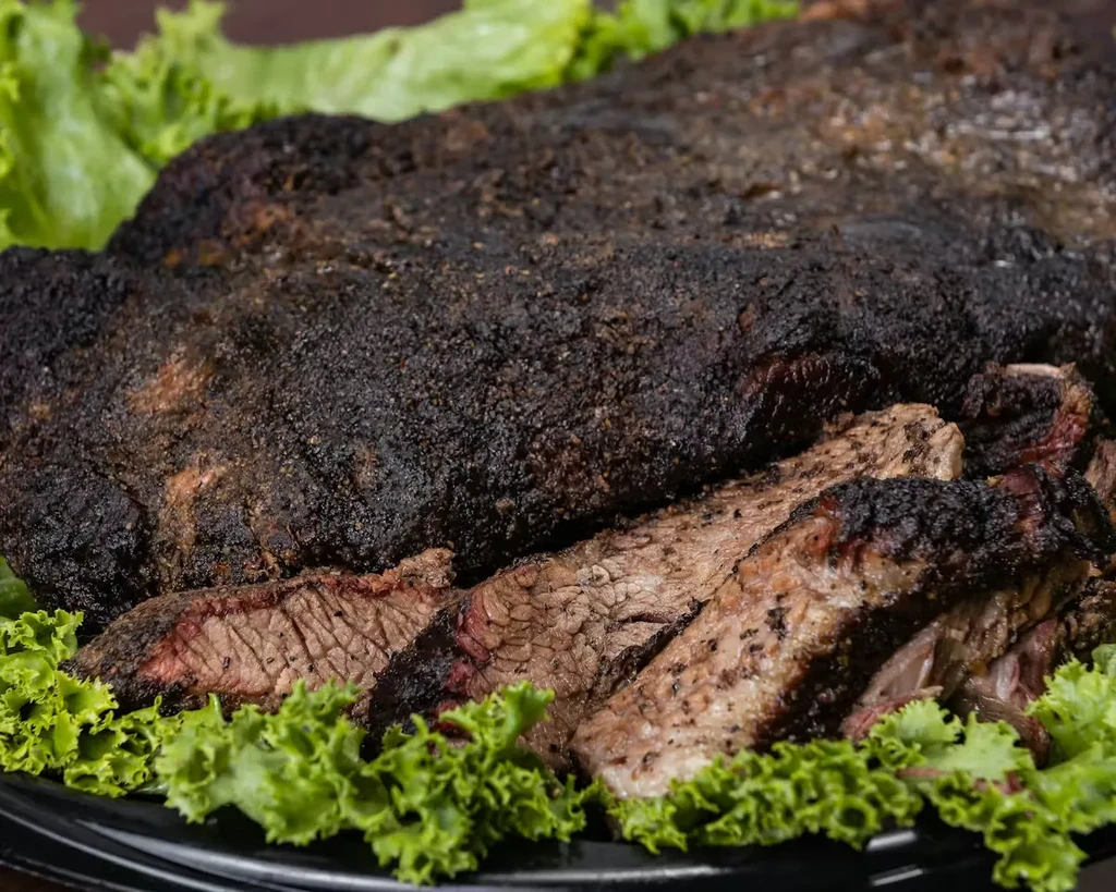 Sliced smoked brisket with bark, smoke rings, and green lettuce.