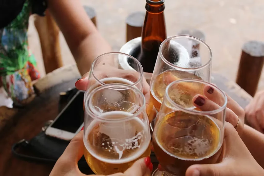Four hands with diverse skin tones toasting amber beer glasses.