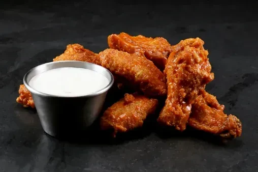 Crispy buffalo chicken wings and white dipping sauce on a dark surface.