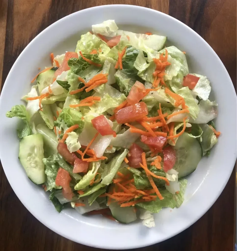 A white bowl of fresh garden salad on a wooden table.