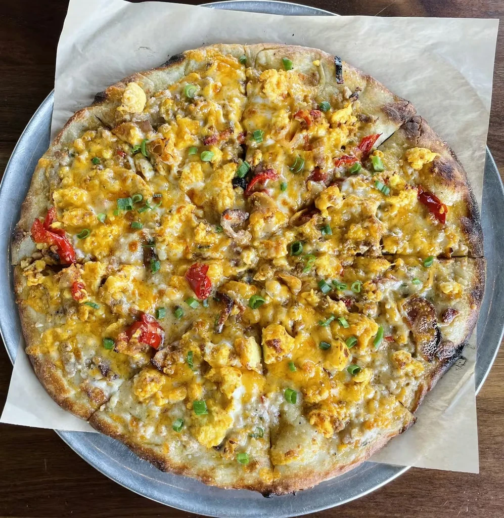 Round pizza with scrambled eggs, melted cheese, peppers, and chives.