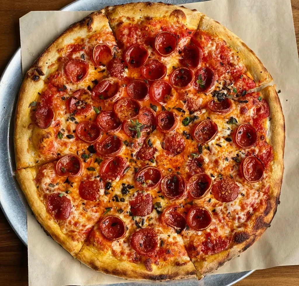 A sliced pepperoni pizza with crispy pepperoni and herbs on a tray.