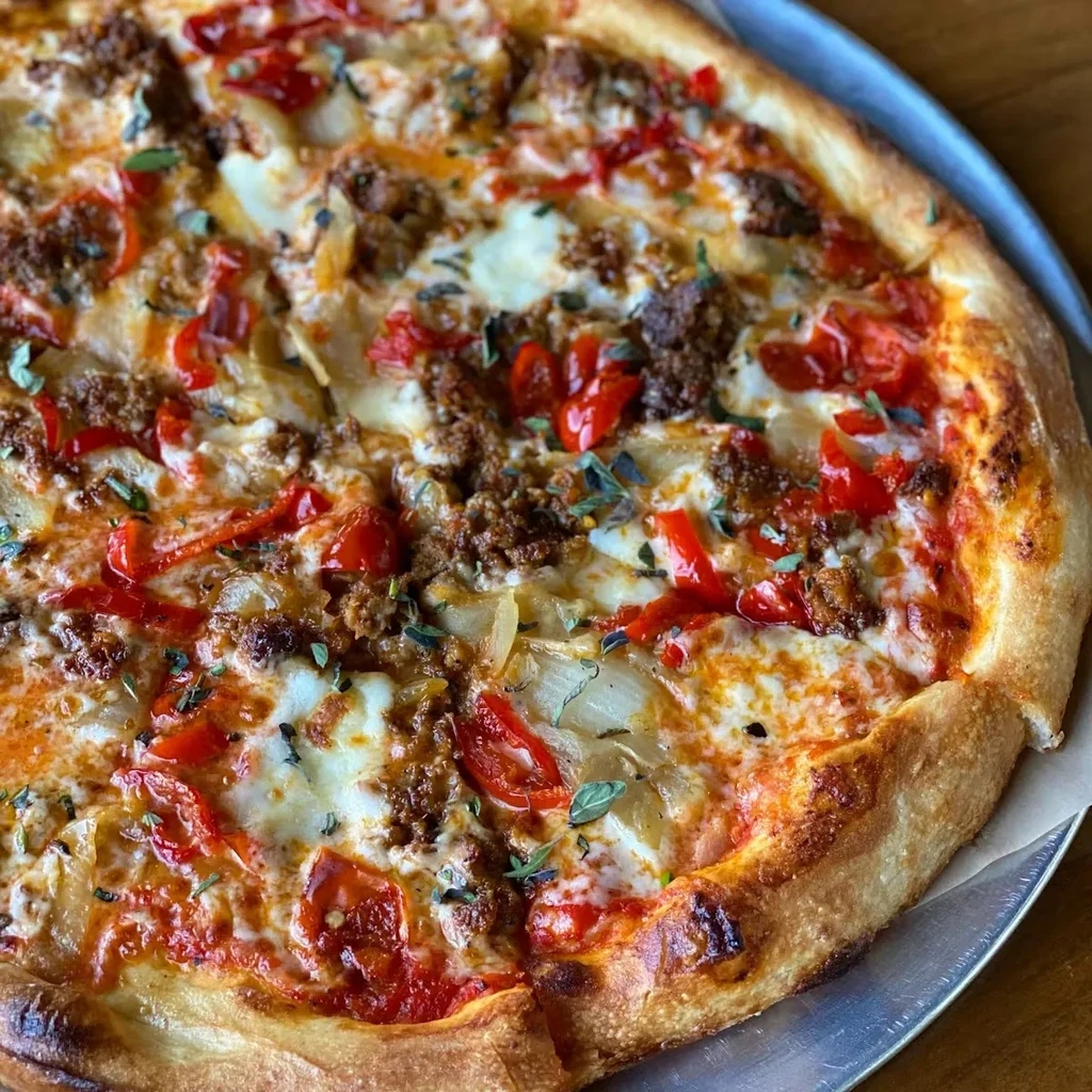 Sliced, freshly baked pizza with meat, bell peppers, onions, and herbs on a pan.