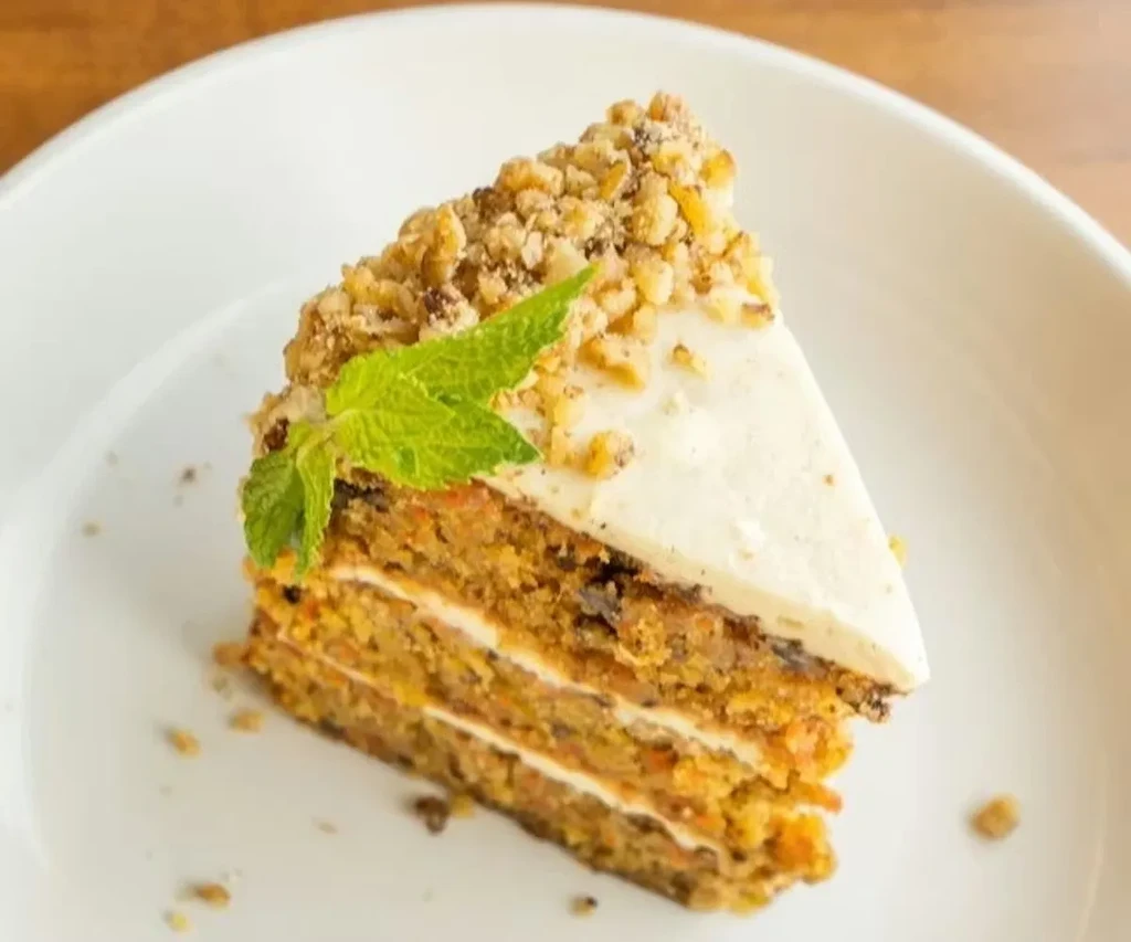 Carrot cake slice with white frosting, chopped nuts, and a mint leaf.