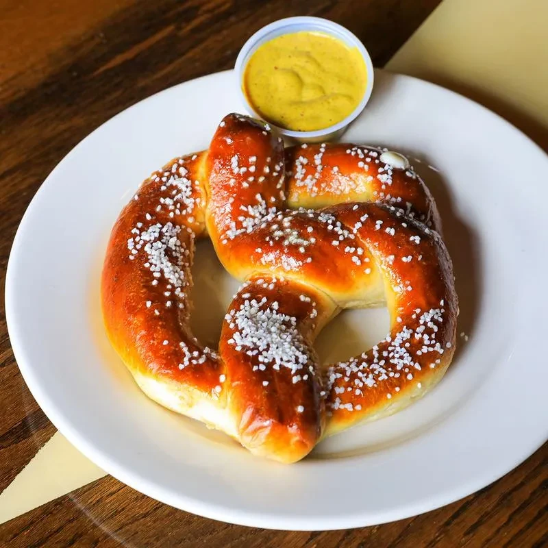 Golden-brown salted soft pretzel with a side of yellow dip.