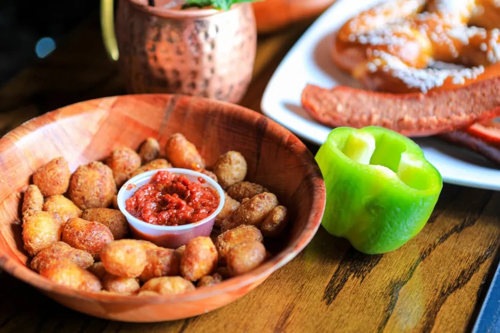 Fried snacks, red sauce, bell pepper, pretzel, and copper mug.