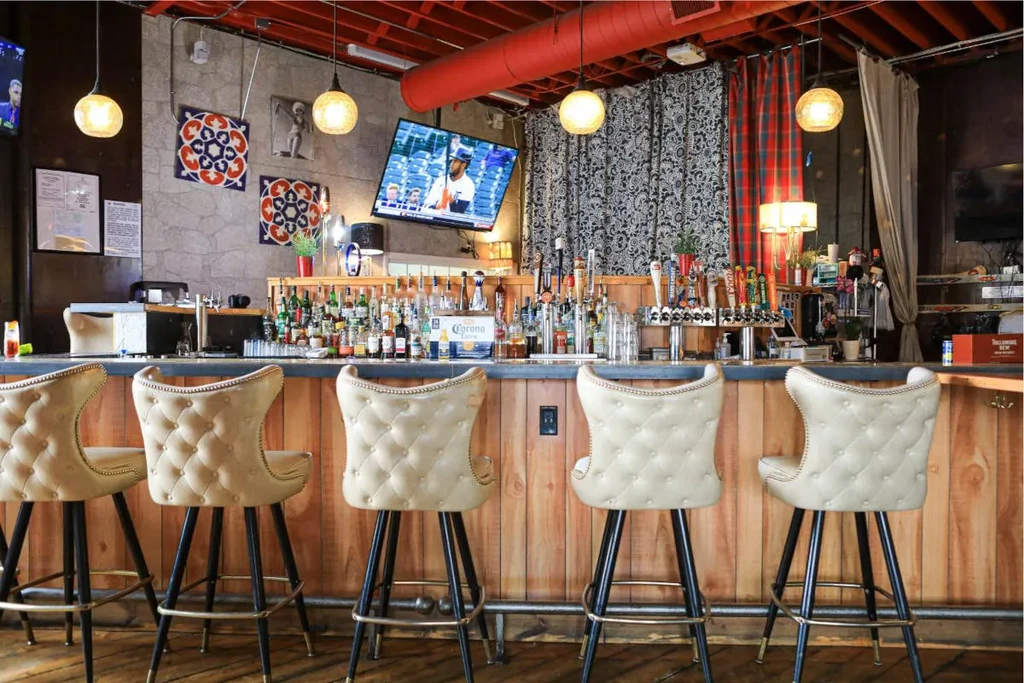 Empty bar stools face a well-stocked bar with sports on TVs.