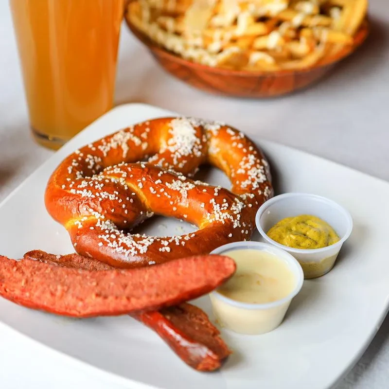 Close-up of a pretzel and sausage plate with two dipping sauces.