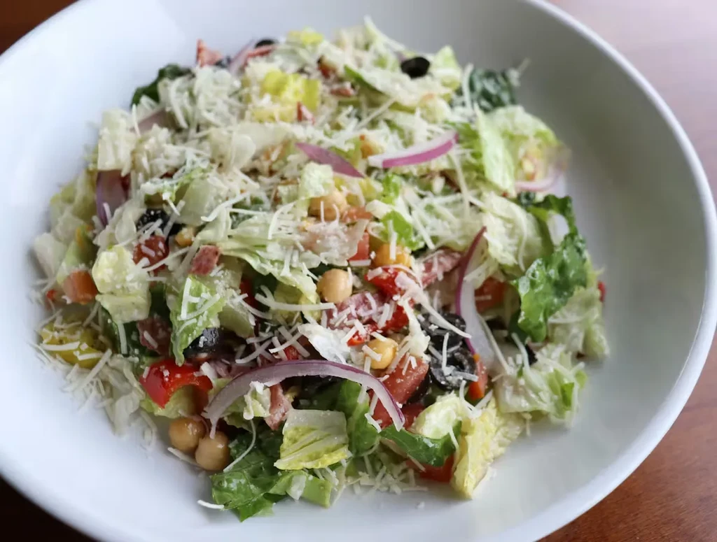 Colorful salad with lettuce, peppers, olives, chickpeas, and cheese.