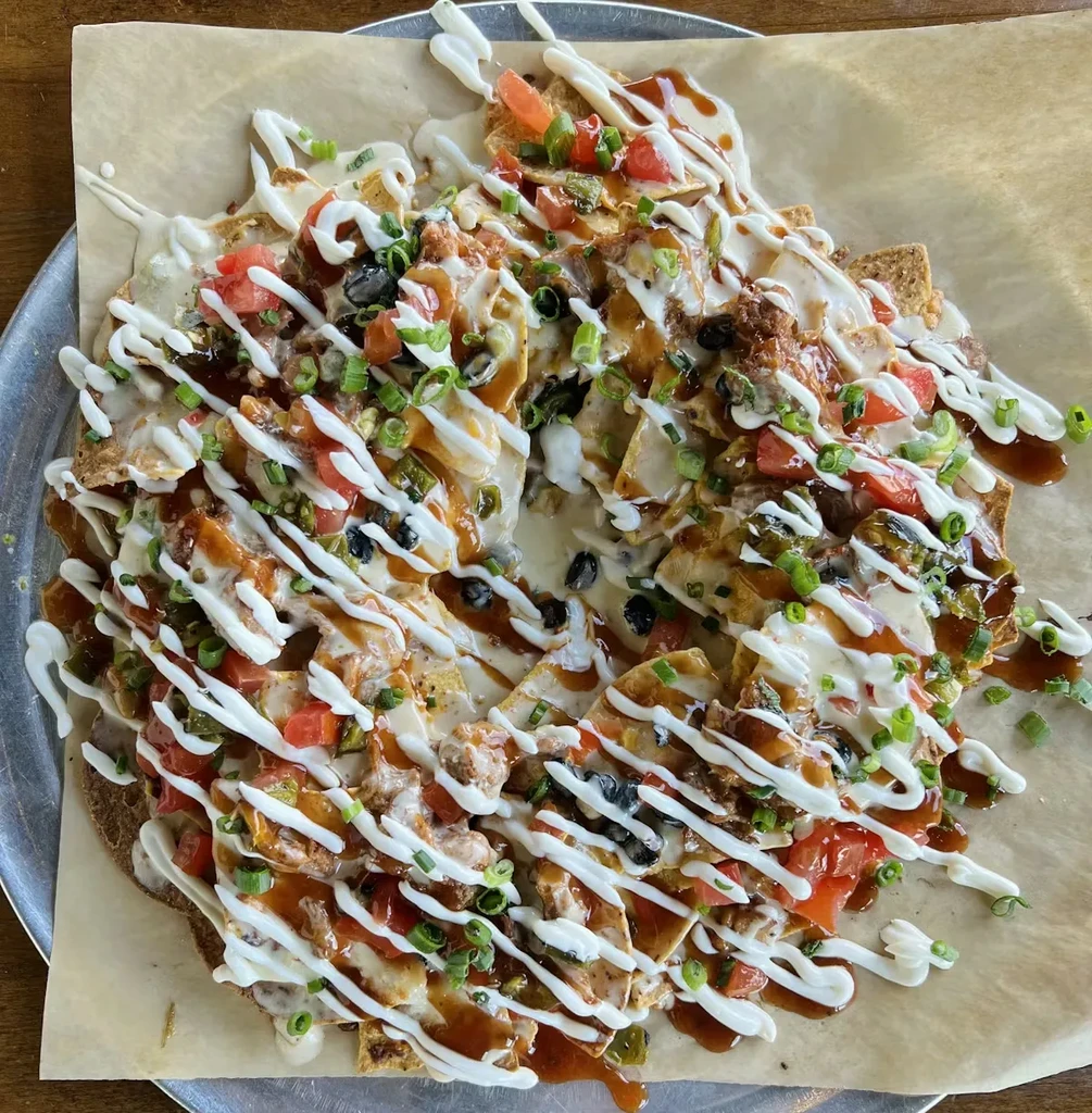 Overhead shot of fully loaded nachos with cheese, meat, vegetables, two sauces.