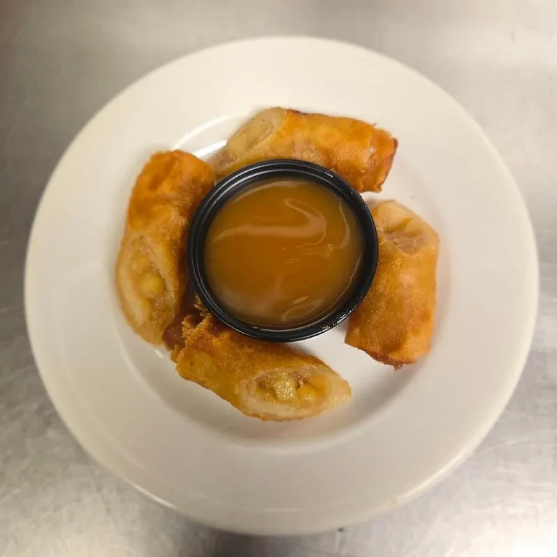 Golden-brown fried spring rolls, one open, with caramel dipping sauce.
