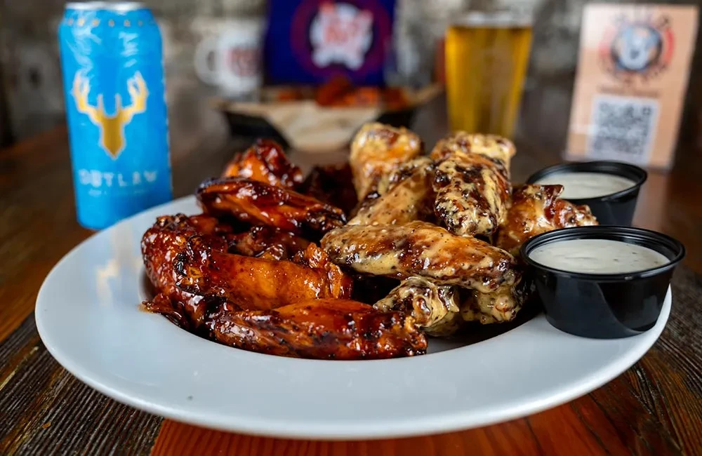 Chicken wings, half dark sauce, half light sauce, with white dips.