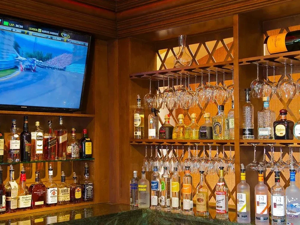 Well-stocked bar with liquor bottles, glassware, and car race on television.