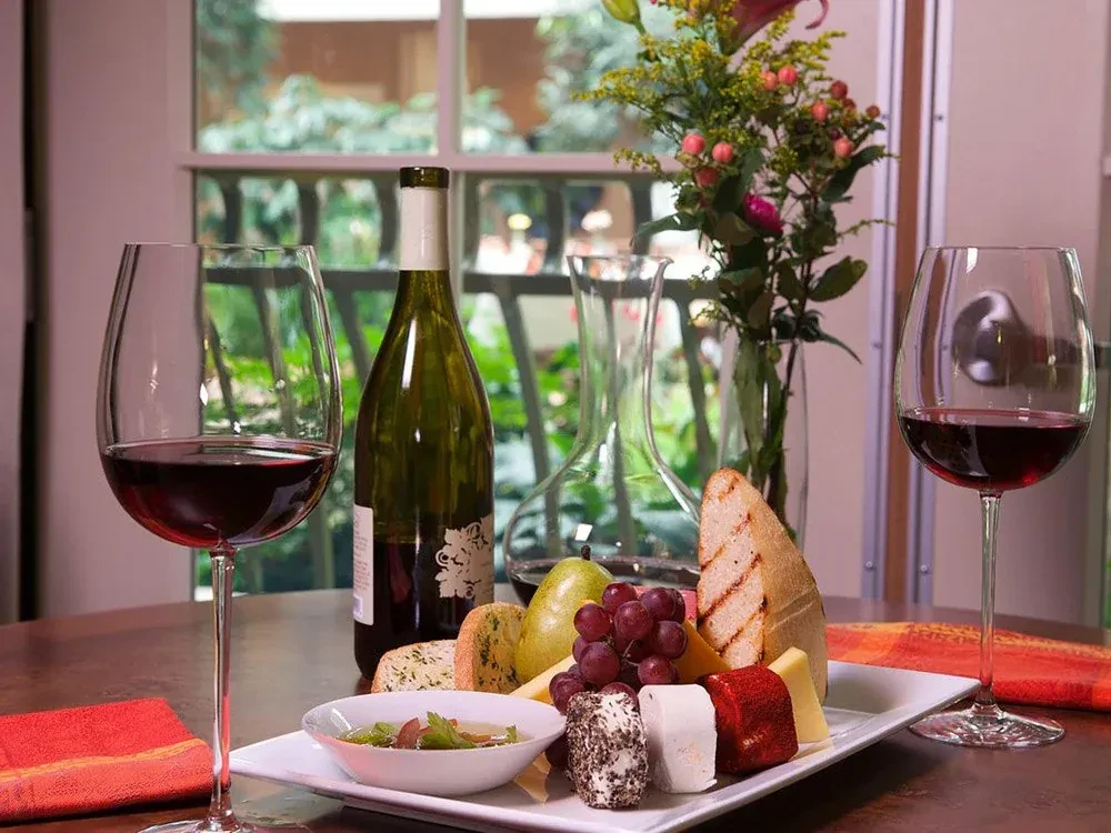 Platter of cheese, fruit, bread, and wine on a wooden table.