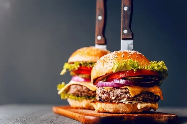Two gourmet burgers with knives on a rustic wooden board.