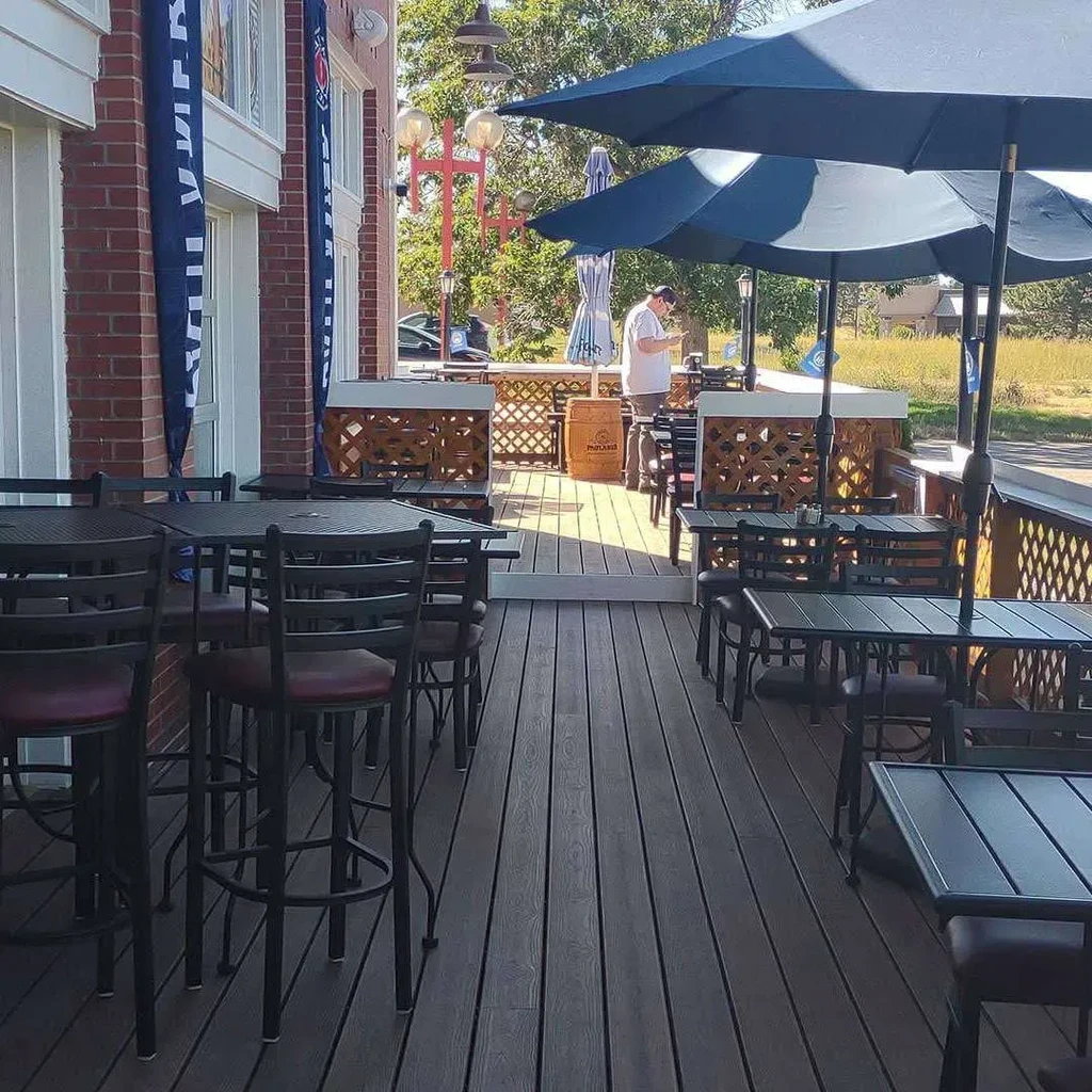 Sunny outdoor patio deck with tables, blue umbrellas, and a person.