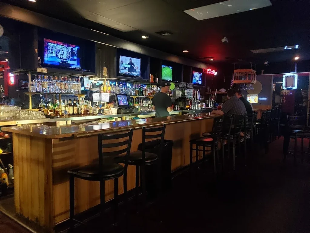Sports bar interior with a stocked bar, multiple TVs, bartender, patrons.