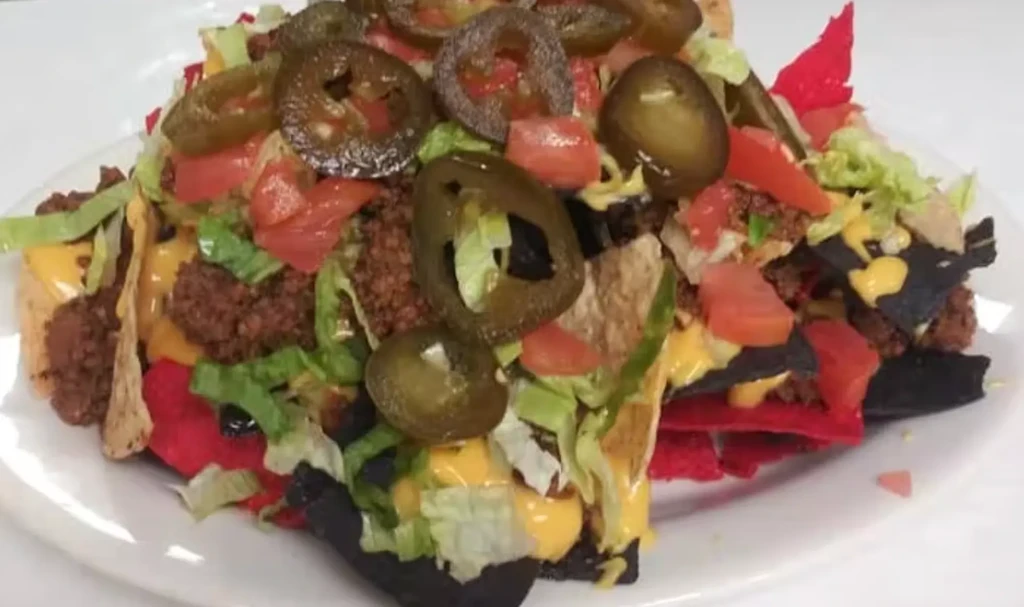 Nachos with diverse chips, meat, cheese, lettuce, tomatoes, jalapeños.