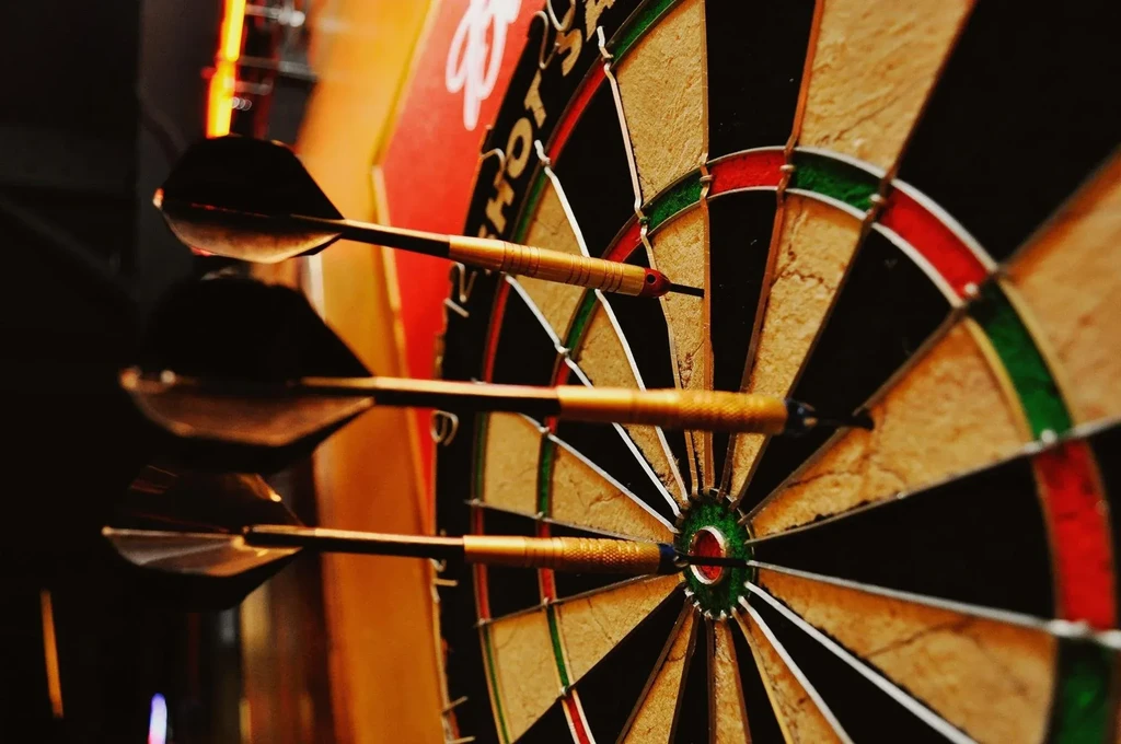 Three darts stuck in a classic dartboard, warmly lit pub setting.