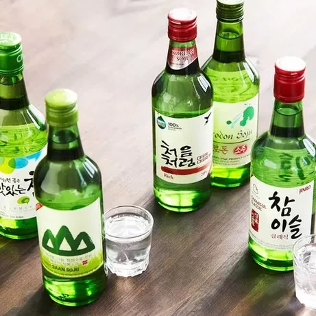 Six green Korean soju bottles and two shot glasses on wooden table.