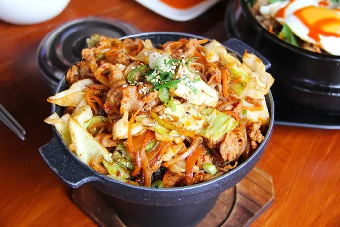 Stir-fried meat and vegetables in a dark bowl, garnished with sesame seeds.