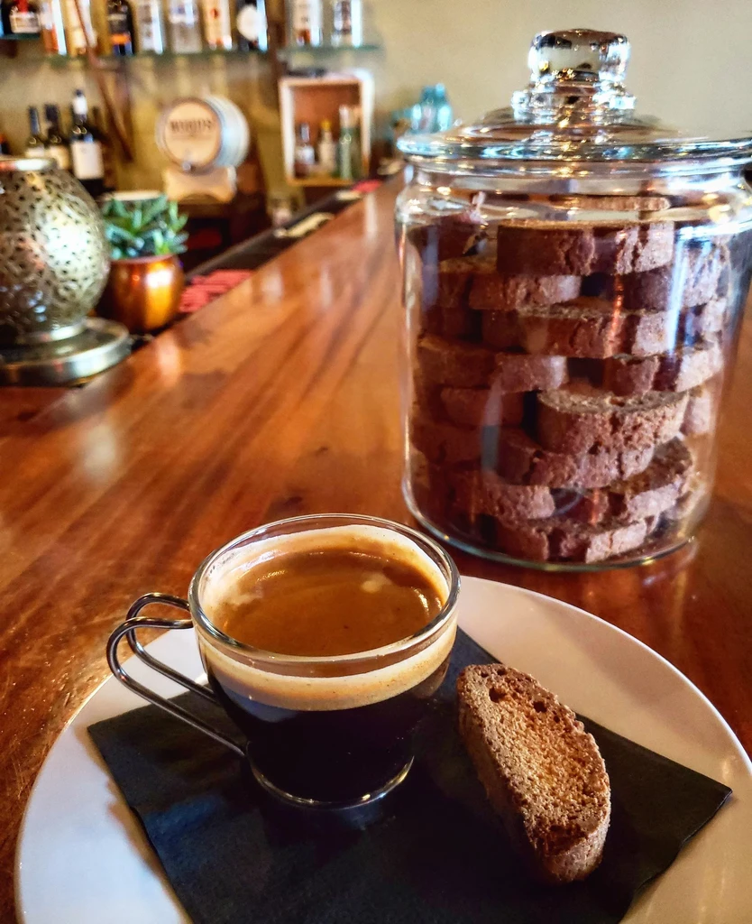 Close-up of espresso, biscotti, and jar on a wooden bar counter.