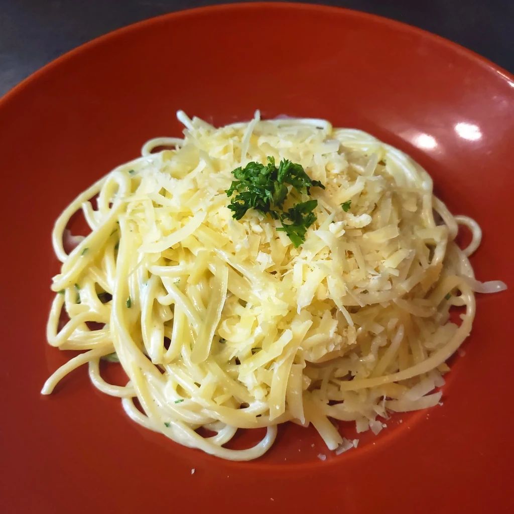 Spaghetti in red bowl with creamy sauce, grated cheese, and parsley.