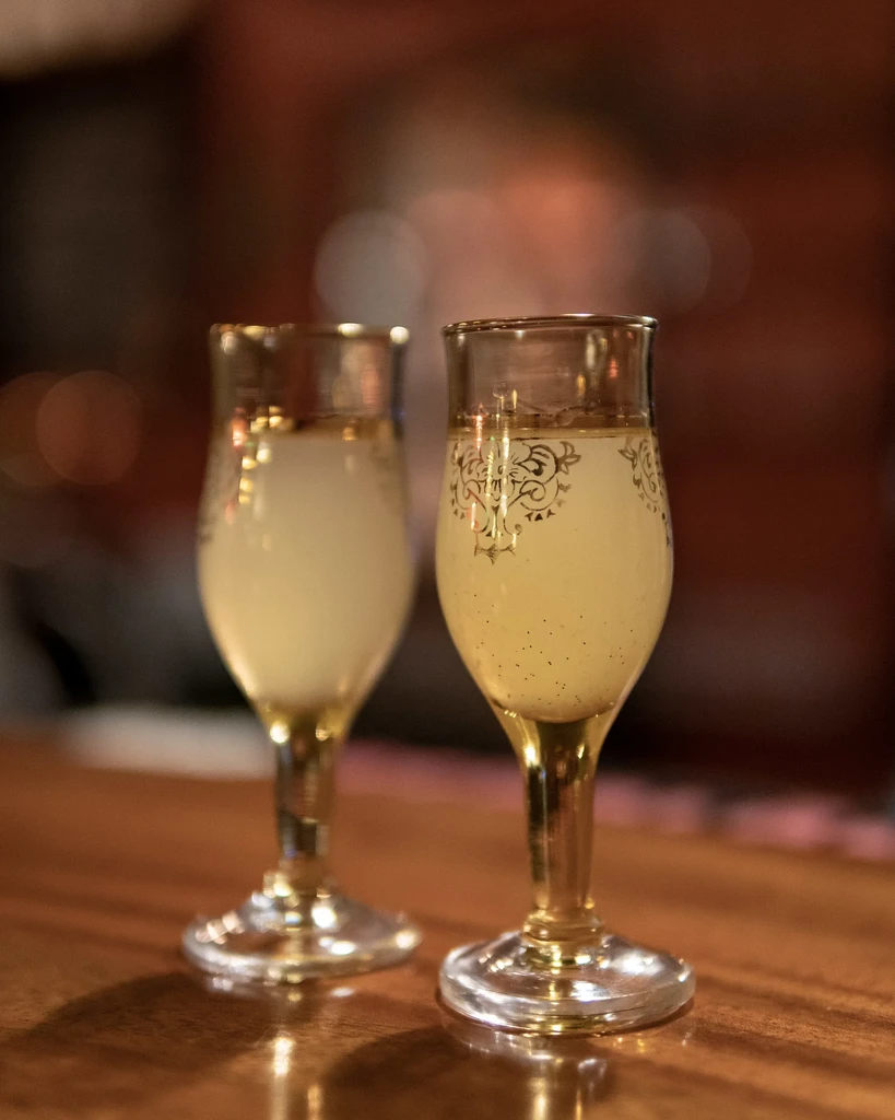 Two elegant stemmed glasses with speckled drinks, gold patterns, on wood.