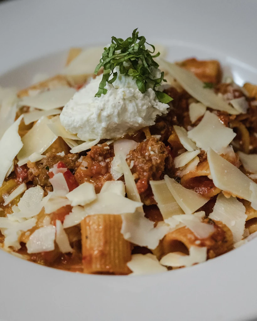 Close-up of rigatoni pasta with meat sauce, Parmesan, ricotta, and basil.