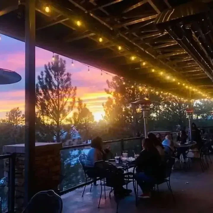 Warm patio with patrons, string lights, and a vibrant sunset.