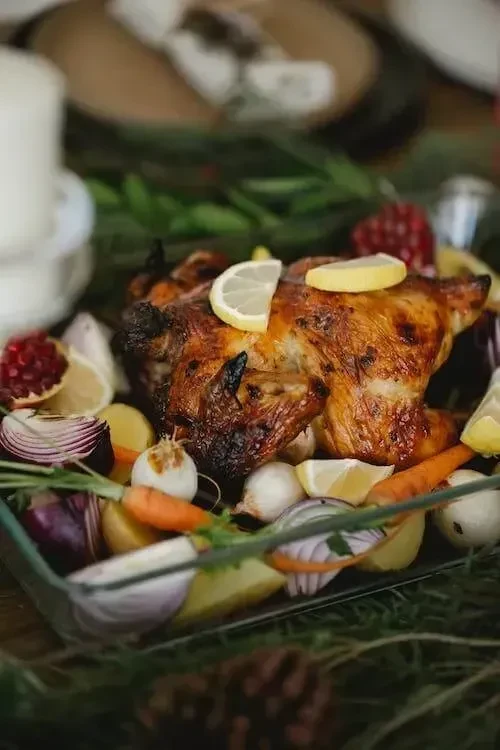 Golden-brown roasted chicken, lemon slices, colorful vegetables, and pinecones.