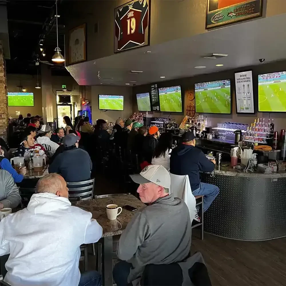 Lively sports bar interior with patrons, large TVs, and sports memorabilia.