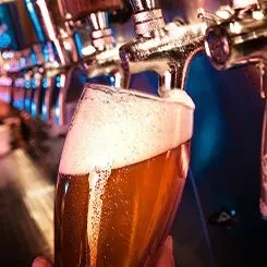Glass of amber beer overflows with foam from a metal tap.