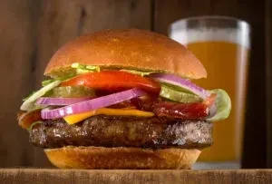 Close-up of a large burger with cheese, bacon, and vegetables.