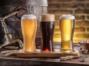Three different beers on a wooden paddle with brewing ingredients.