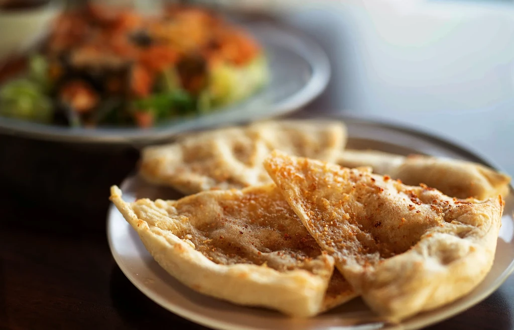Golden-brown flatbread pieces on a white plate, with a soft-focus salad.